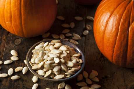 pumpkin seeds in a bowl with pumpkins next to it