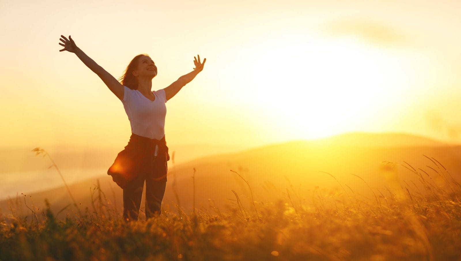 woman with arms up at sunset