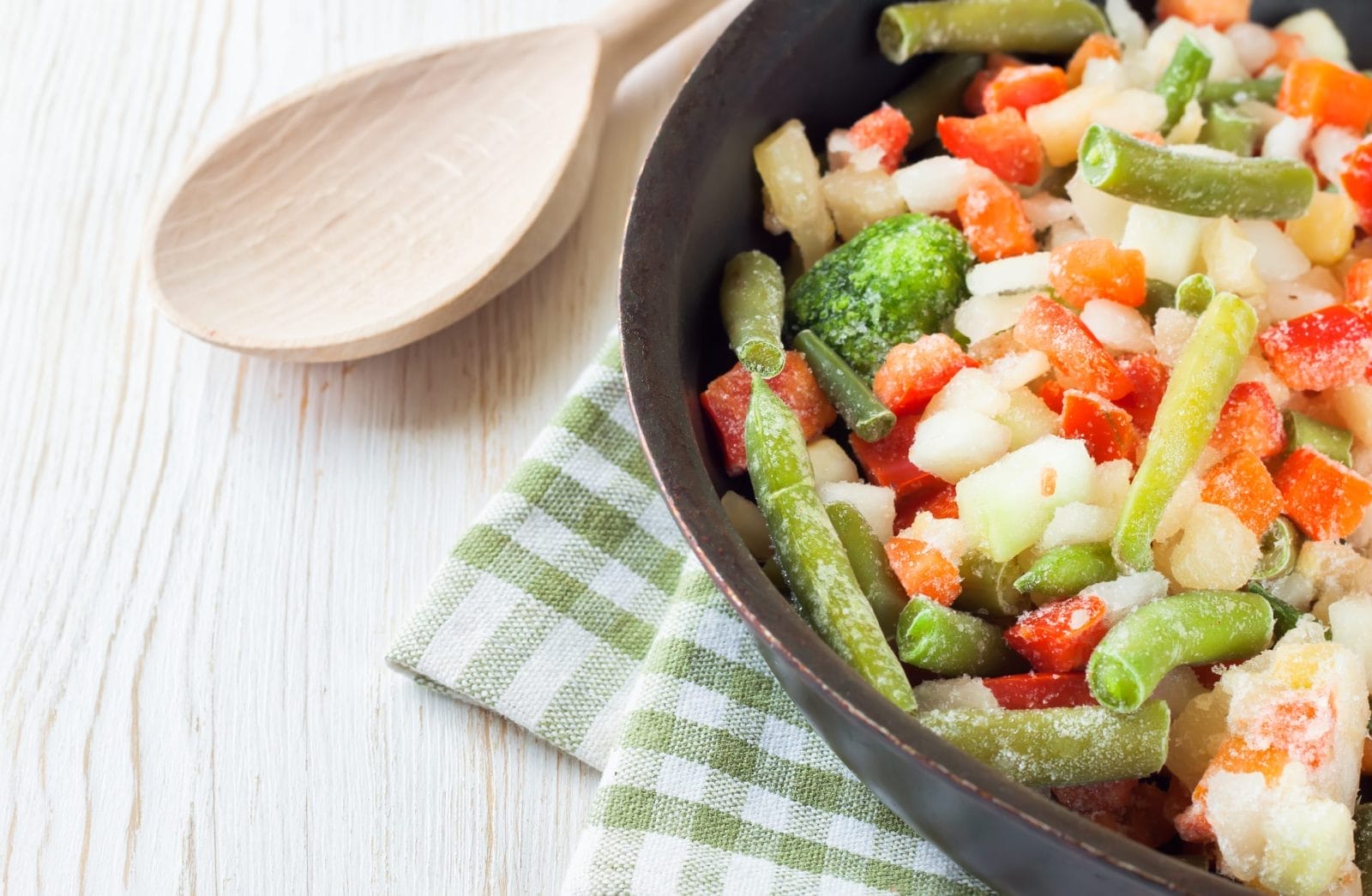 Frozen vegetables in pan next to wooden spoon