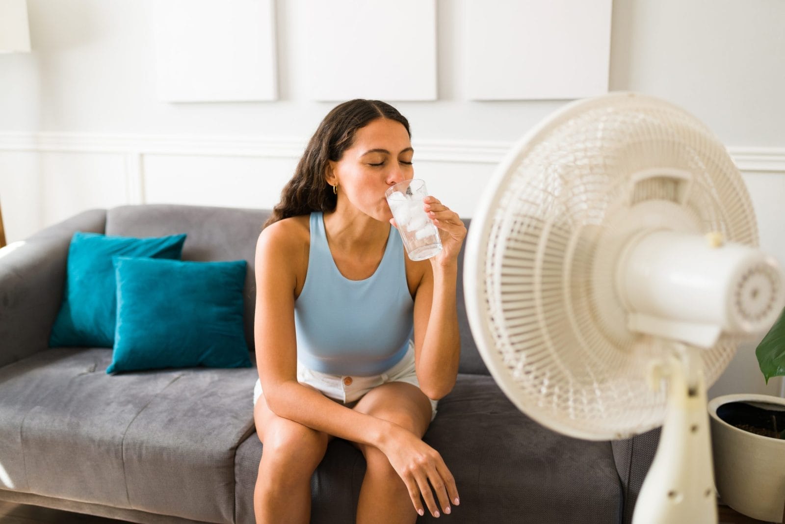 Woman trying to cool down drinking water with a fan on