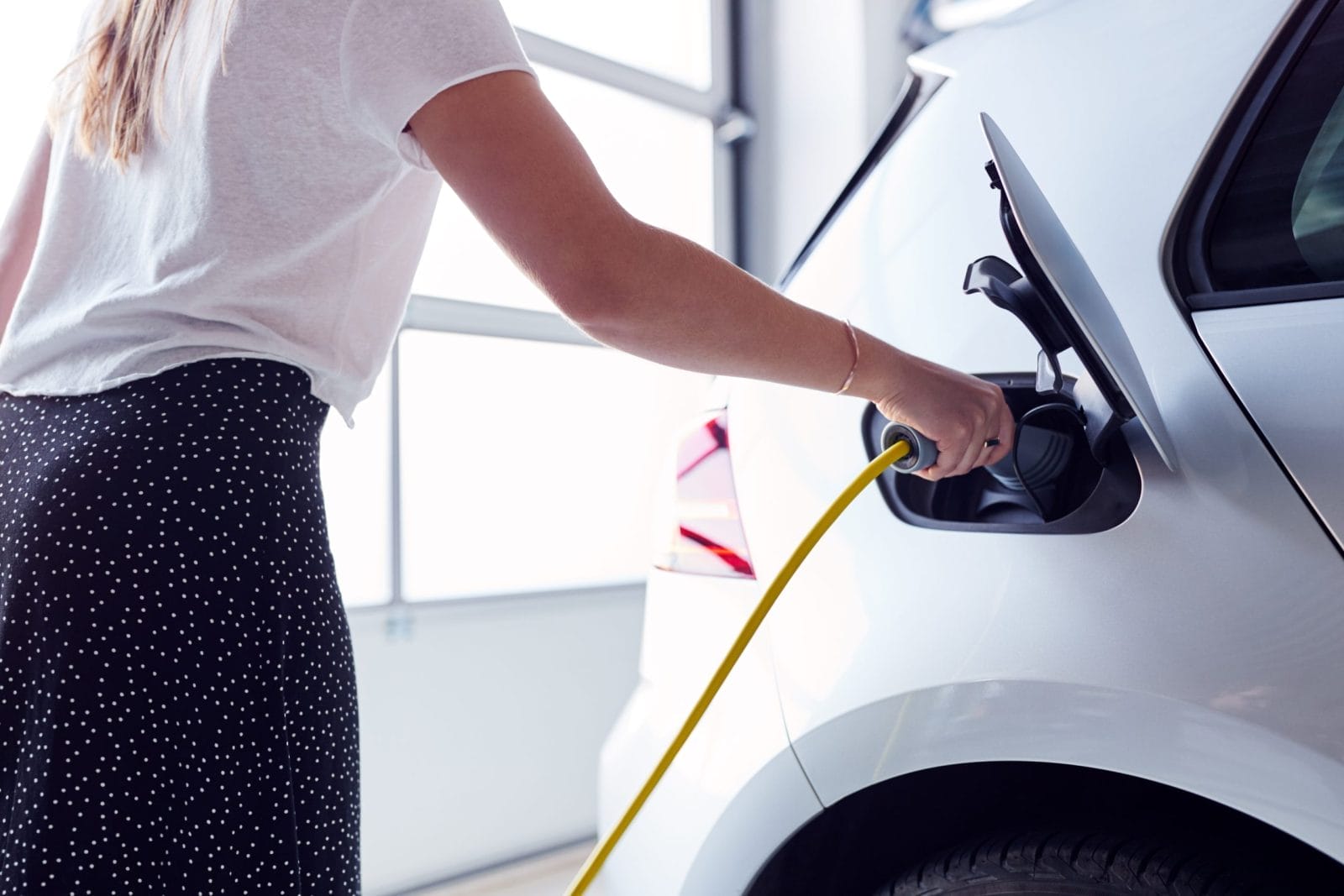 Woman Charging Electric Vehicle With Cable In Garage