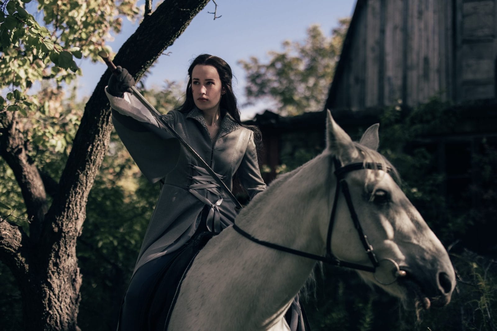 Young woman in image of ancient rider warrior sits on white horse with sword