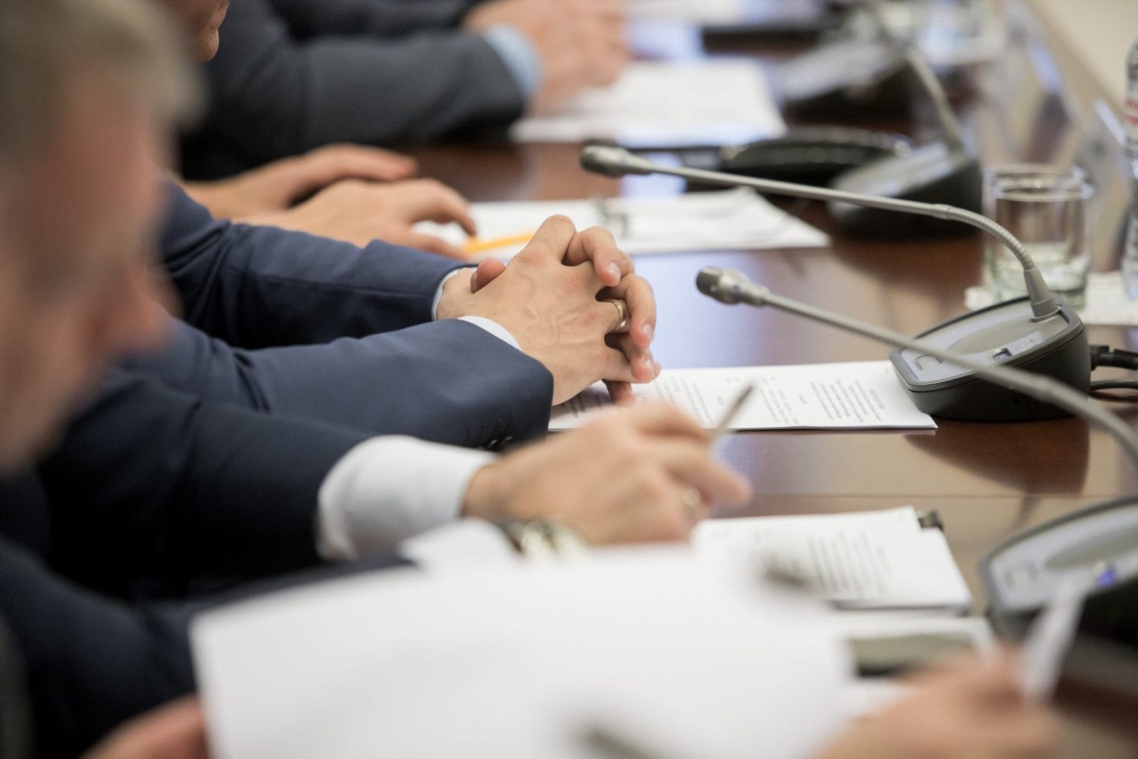 Politicians sitting at table with microphones and papers covering it