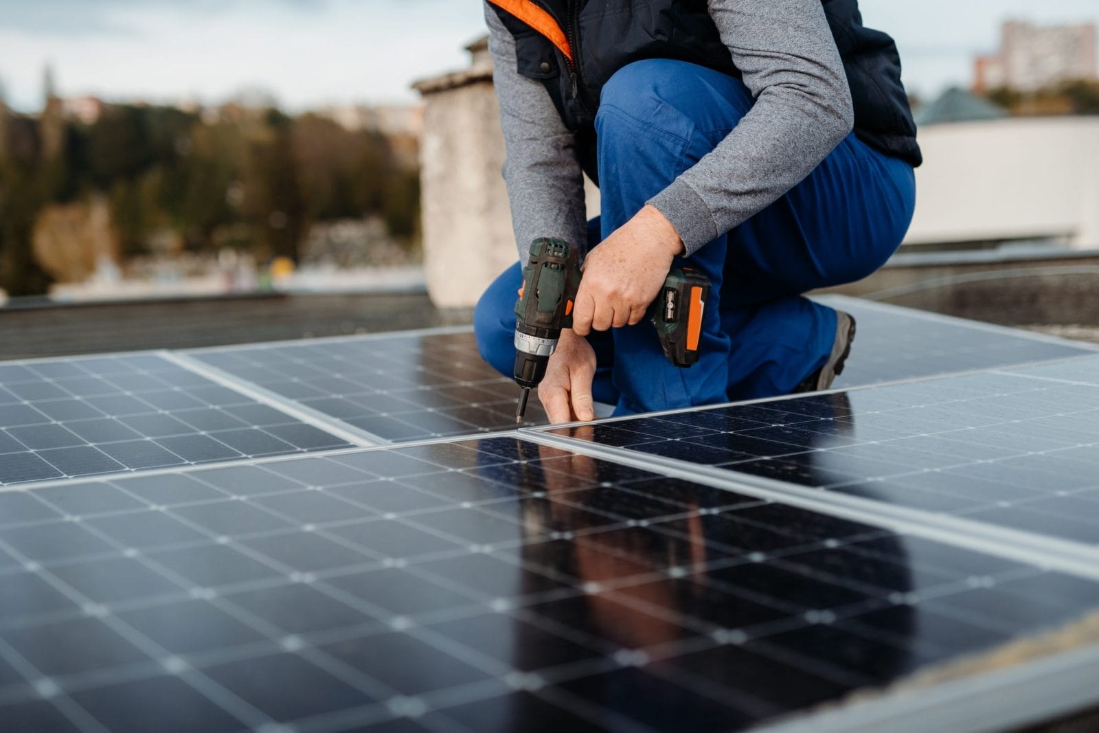 Man with drill installing solar panels on roof on family house a sunny day