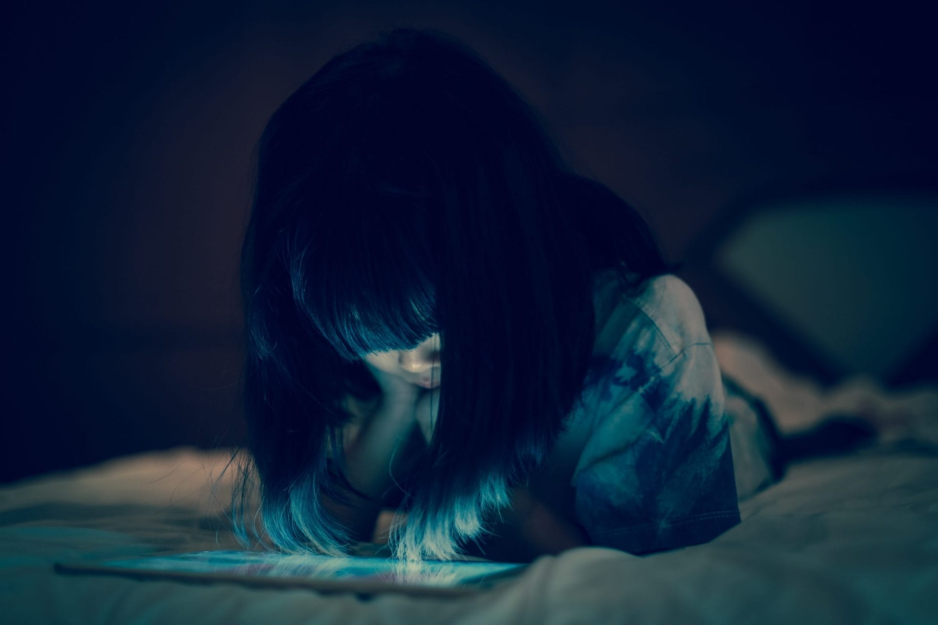 Girl lying on bed and looking down at a tablet