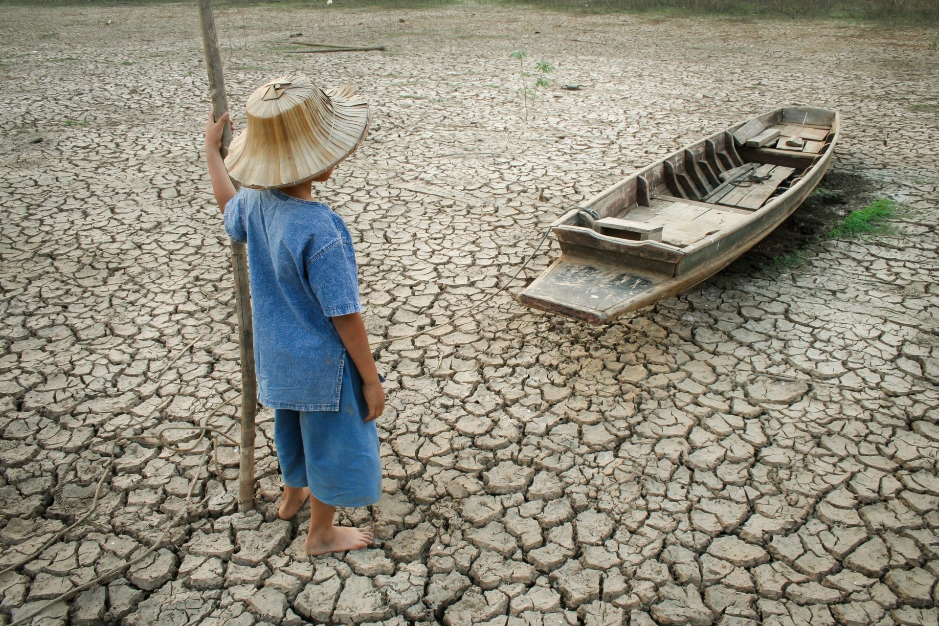 Child standing on dry and cracked ground next to boat