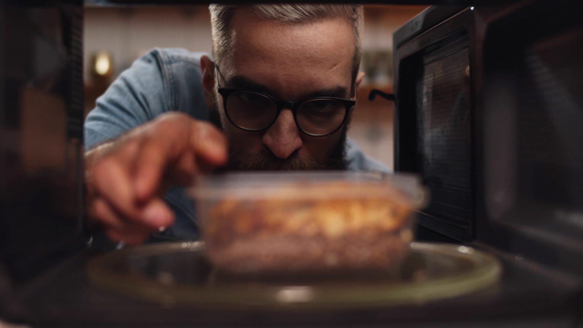 Man reaching into microwave to grab plastic container of food
