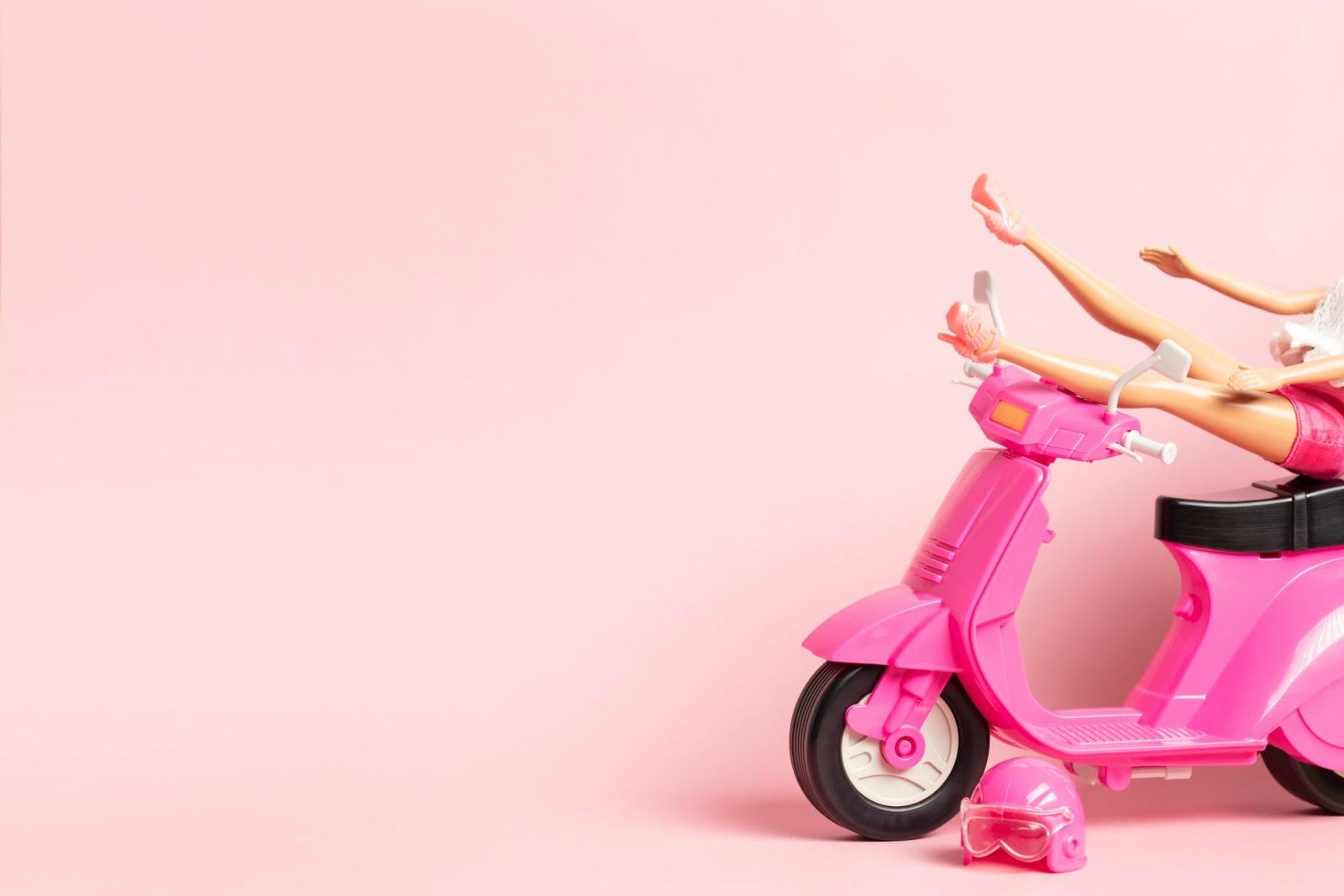 Barbie doll legs on top of pink moped against pink background