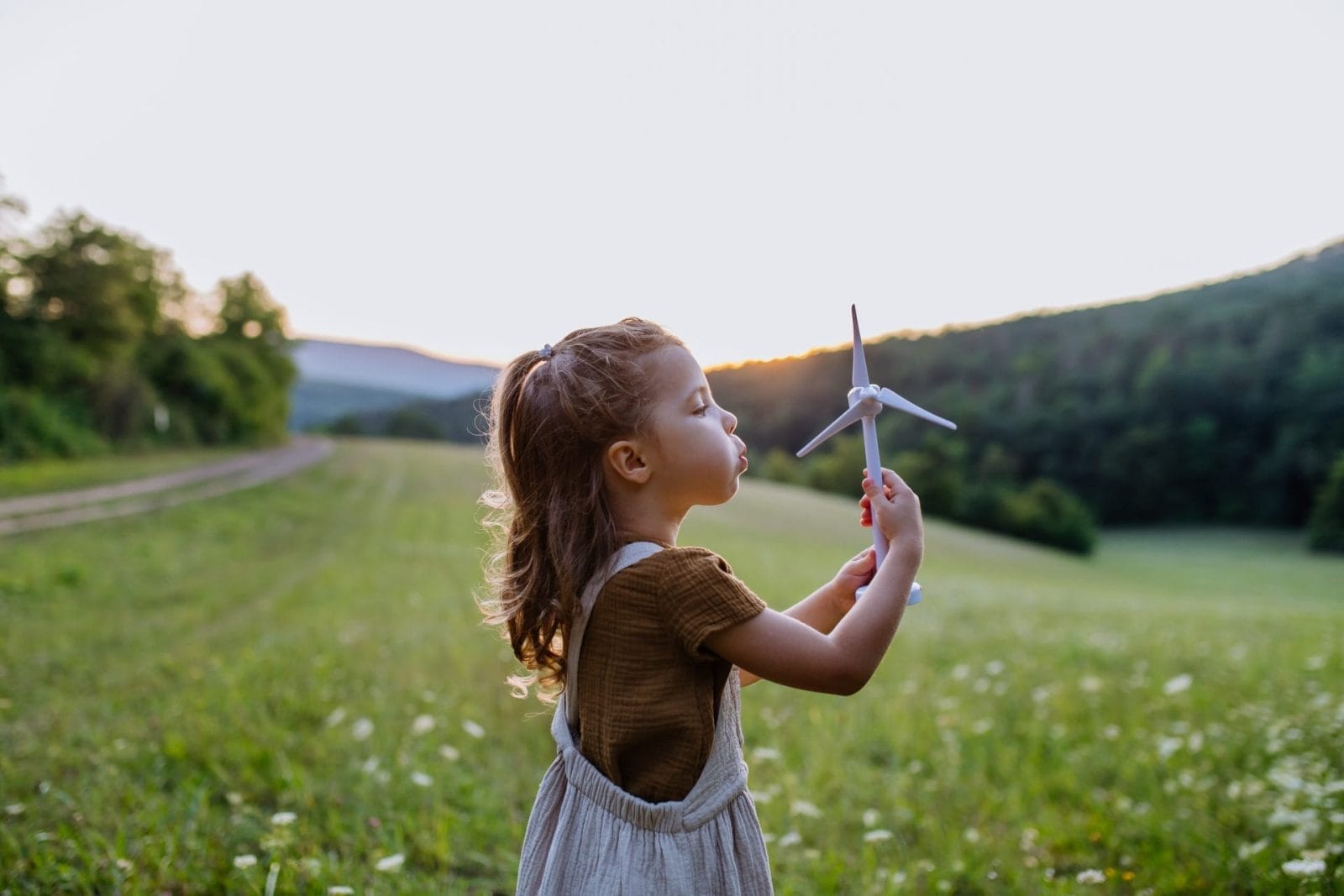 young person blowing on model windmill in field. climate change awareness young people