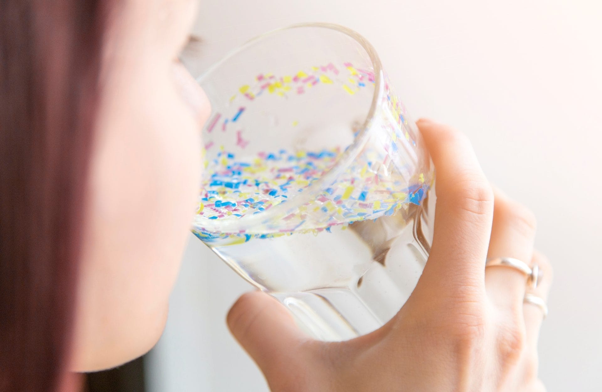 Girl drinking glass of water filled with tiny bits of plastic
