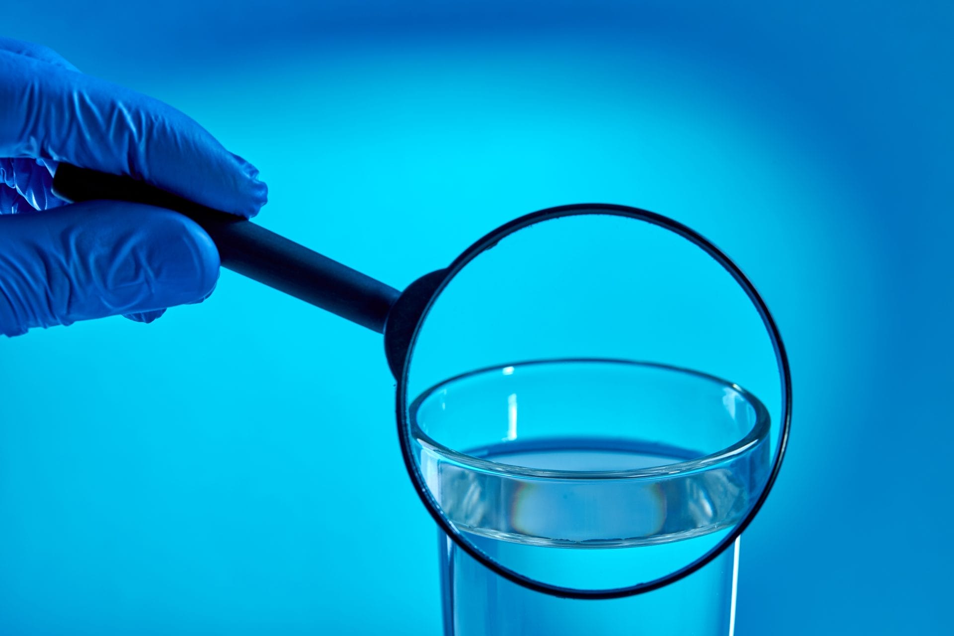 A person holding a magnifying glass next to a cup of water