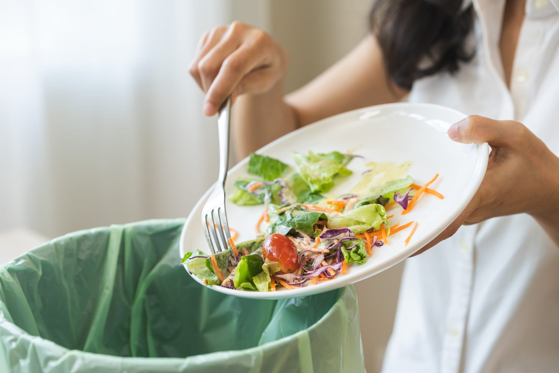 Woman scraping salad off plate into compost bin