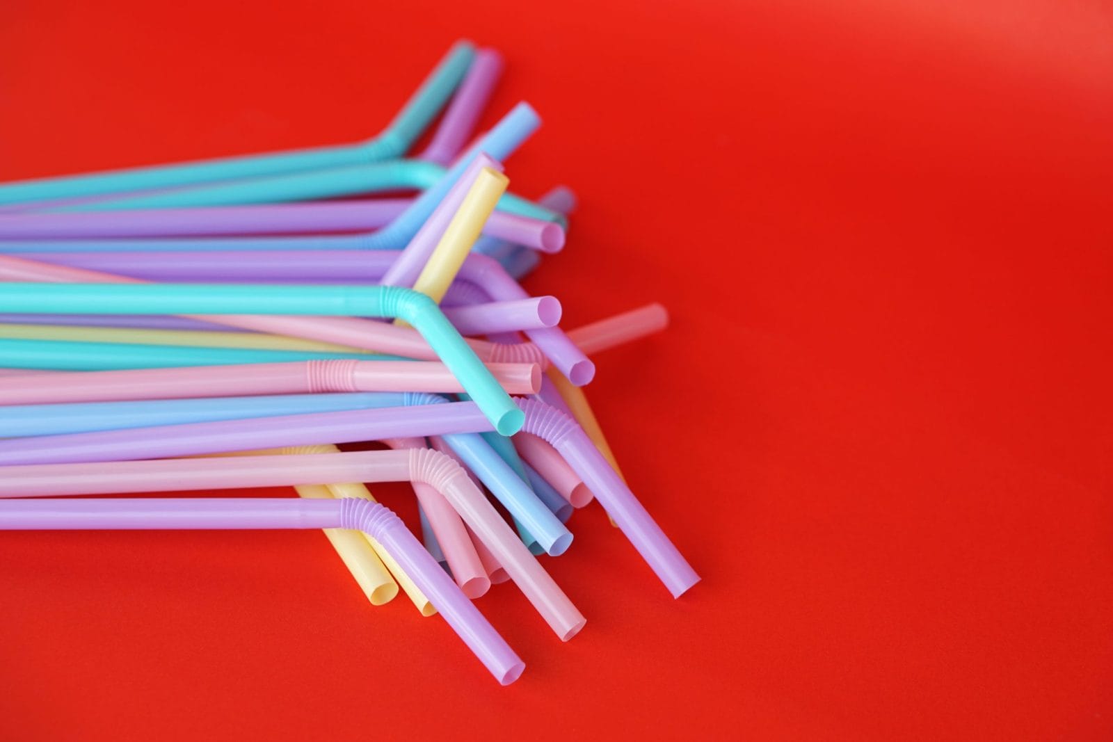 Colorful plastic drinking straws tubes for juice and cocktails, red background