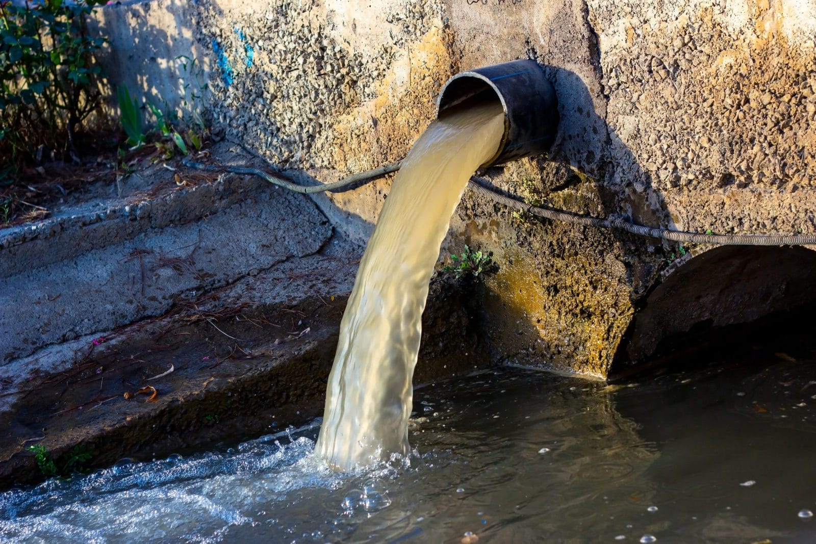 Wastewater sewage pipe dumps the dirty contaminated water into the river. Water pollution, environment contamination concept