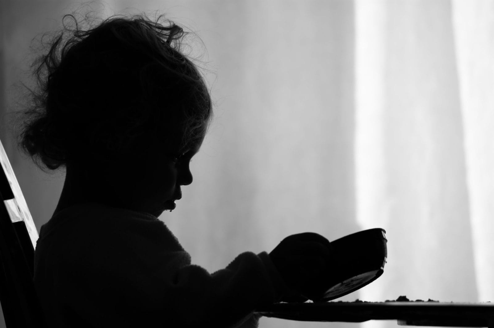 A two year old girl is sadly looking into her empty bowl wishing she had more to eat. / Hunger