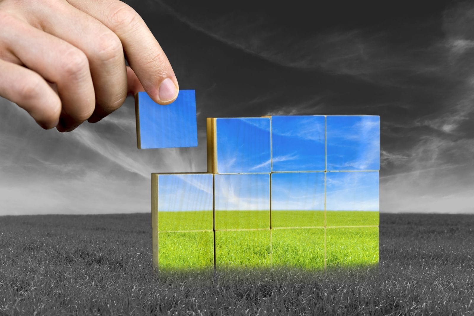 Male hand placing last piece of a cube of color grass field. Ecological or positive concept.