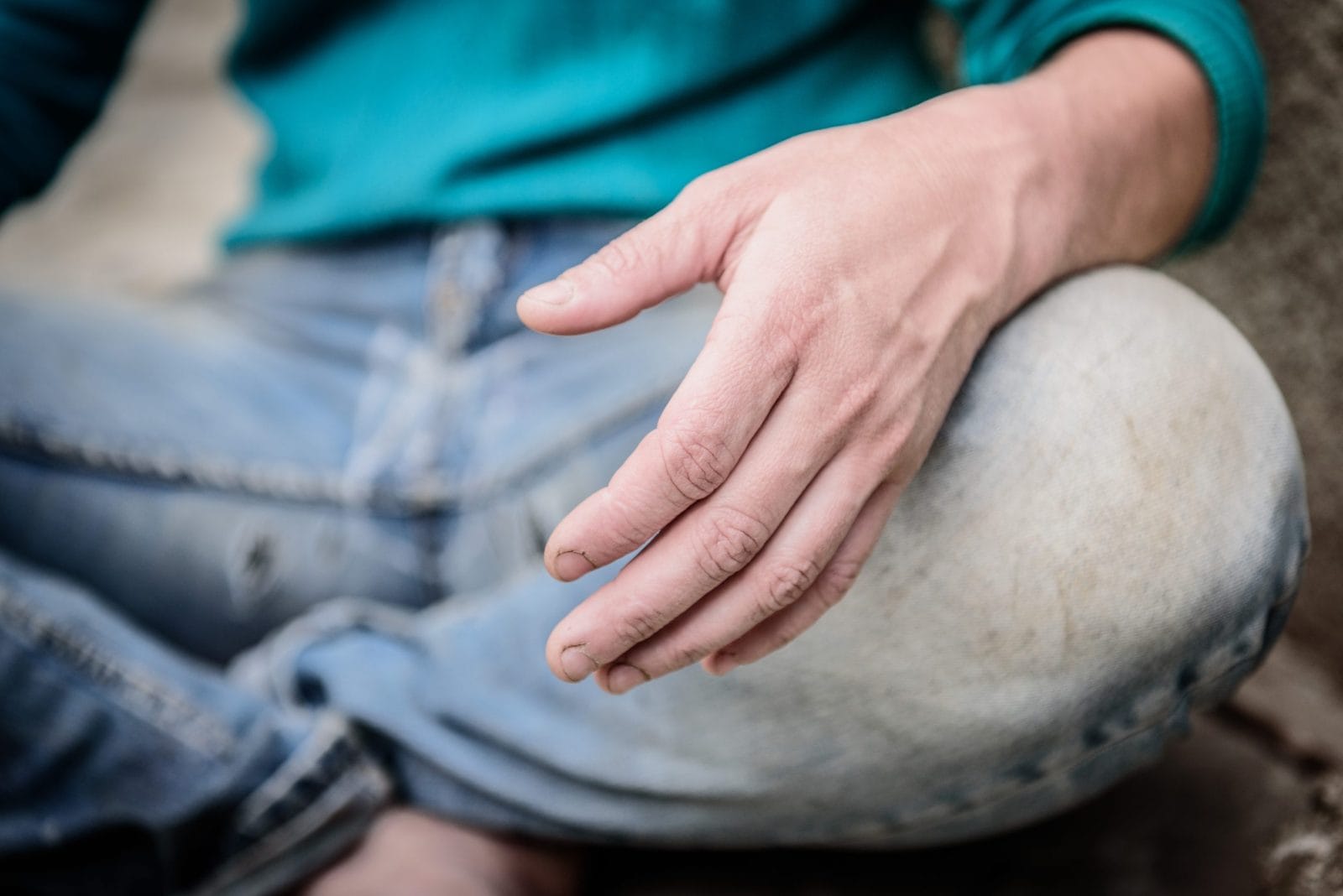 Hand of homeless beggar asks for alms, help, money and food on concrete. Beggar begging on the street. Poverty concept. Unemployed human in torn clothes sitting on the ground.